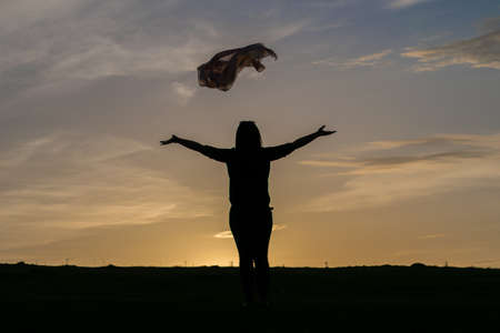 Silhouette of a woman standing in a field at sunset, skyの写真素材