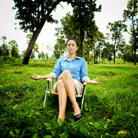 Business woman meditating and making yoga at green fieldの写真素材