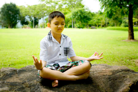 Boy in a lotus pose meditation and yoga on the rock in public parkの写真素材