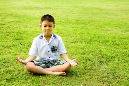 Boy in a lotus pose meditation and yoga on the grass in public parkの写真素材