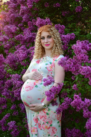 pregnant girl smiling in a blooming spring park, the girl is walking in a  syringa vulgaris flowers parkbushes of lilacの写真素材