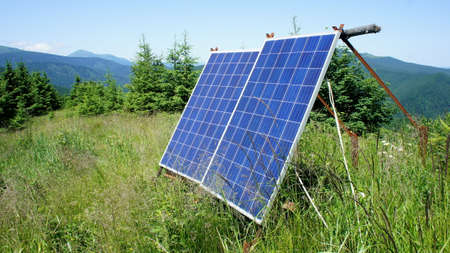solar panels high in the mountains. solar panels, green grass and spruce on a background of mountains in summerの写真素材