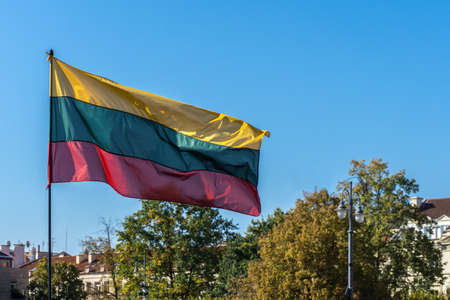 Lithuanian flag waving in blue sky over buildings and trees in Vilnius, capital of Lithuaniaの写真素材