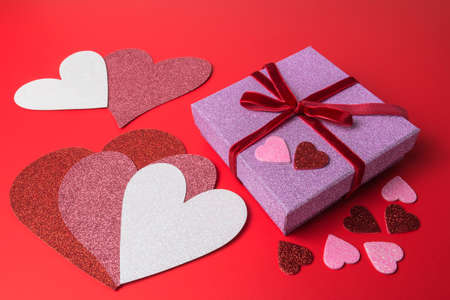 Pink paper gift box and heart shapes on red paper background