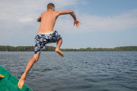 Young man jumping from boat into lake waterの写真素材