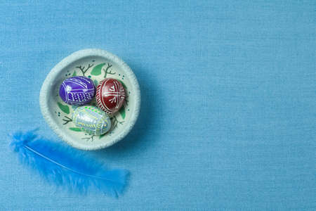 Mix of colored wooden eggs with the traditional designs on painted plate, blue cloth background for copy spaceの写真素材