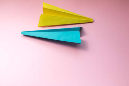 Blue and yellow paper planes on pastel pink paper background, place for copy spaceの写真素材