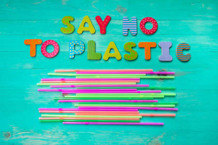 Say no to plastic - wooden letters phrase on wooden background with plastic straws, top view. Ban...