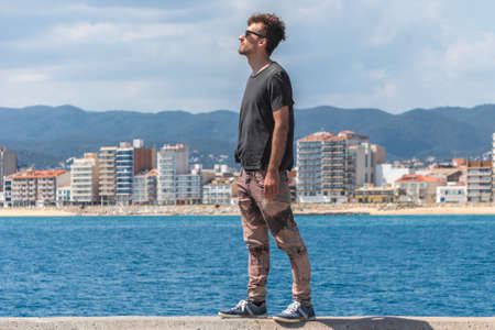 Young man standing on sea pier and looking ahead, expressing happiness and freedom. Man on seascape...
