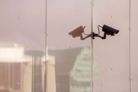 CCTV camera on toned glass wall of a building with reflection of modern city buildings. Security...
