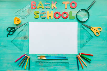 Back to school concept. Flat lay of wooden turquoise background with text of colorful letters, blank, school supplies, and autumn dry leaves. Copy space. School education and September 1 concept.の写真素材