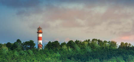 Panoramic view of lighthouse in forest at dusk sky background showing way for ships in seaの写真素材