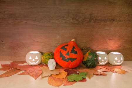 Decoration of Halloween colorful pumpkin heads, burning squash shape lanterns, skull-shaped toy, and dry autumn leaves on wooden background. Halloween concept.の写真素材