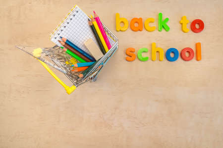 Back to school concept. Flat lay of school supplies in shopping cart on wooden background with text...