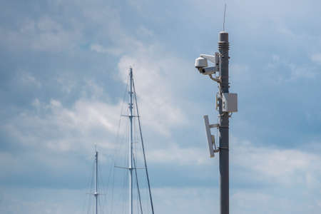 CCTV cameras installed on pole in cloudscape and yacht masts background in seaport. Video equipment outdoor safety system area control and copy space.の写真素材