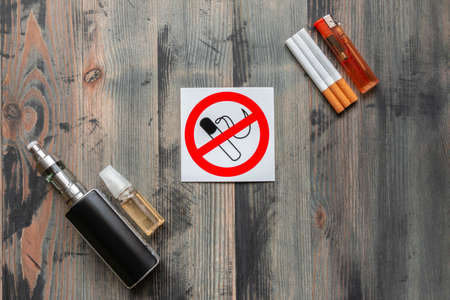 Black e-cigarette, sweet e-liquid, tobacco cigarettes with lighter and sign stop smoking on grey wooden background. Top view. Stop smoking conceptの写真素材