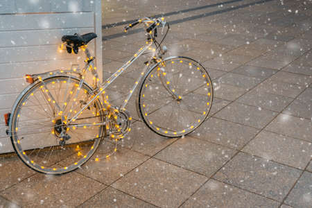 Christmas bicycle. Vintage white bike decorated with Christmas lights on Christmas fair during...