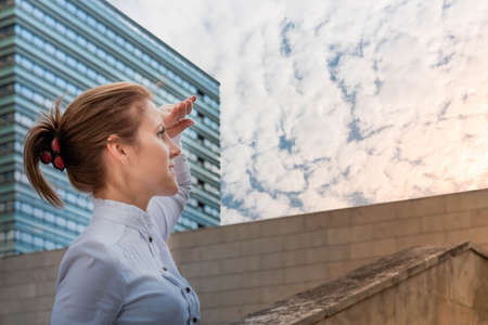 Attractive woman standing on urban background and looking ahead to sunny sky. Successful woman concept. Copy spaceの写真素材
