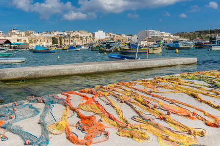 Traditional colorful Maltese fishing nets on concrete pier. Fishing nets left for dry in Marshallock...
