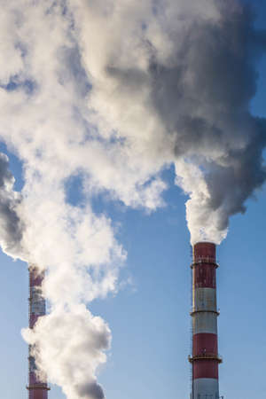 Three factory pipes with thick smoke on blue sky background. Air pollution. Ecological problem. Copy...