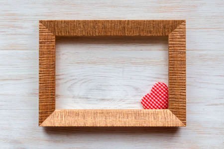 Wooden frame for photo, picture or text and handmade red checkered heart in corner on vintage wooden white painted wall background. Retro style Valentine's day background. Copy space.の写真素材