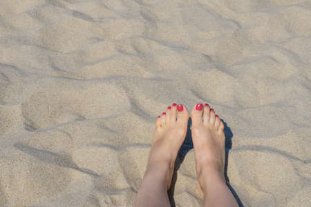 Female feet on beach sand. Woman's feet with red nails on seashore sand background in sunlight near...