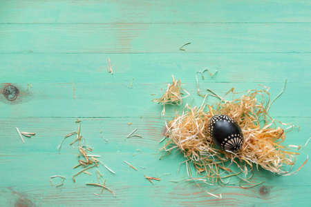 Wooden black painted patterned Easter egg and hay straws around on wood backgroundの写真素材