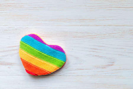 One rainbow heart shape pillow on white painted vintage wooden background. Symbol of homosexual love rainbow heart. Valentines Day concept. Background with copy space for LGBT. Top view, flat layの写真素材