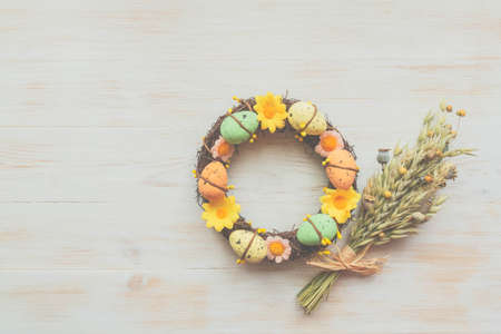 Easter eggs and flowers wreath dry wheatgrass, next to flower bouquet on vintage wooden background