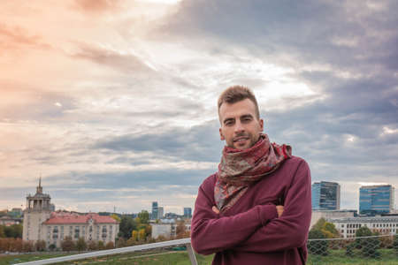 Portrait of handsome man with crossed arms at dramatic sky and urban background. Attractive guy...
