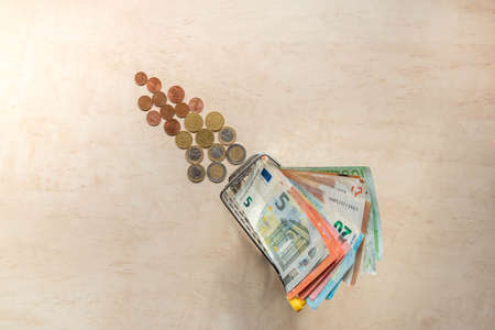 Euro banknotes in small shopping cart and euro coins on background. Miniature shopping trolley with cash. Money of euro area. Copy space. Top view. How to make big money from small money concept.の写真素材