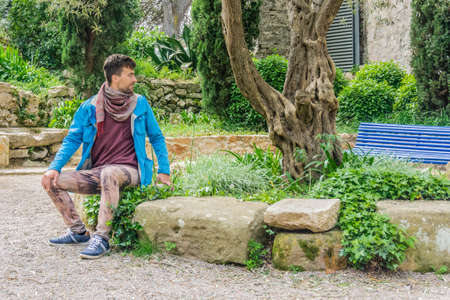 Man with blue jacket sitting on bench in city park. Alone man alone outdoors in park. Hansome guy...