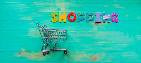 Empty shopping cart and inscription SHOPPING on green wood background. Word shopping and trolley from one side. Concept of online shopping. Web banner. Horizontal orientation. Top view.の写真素材