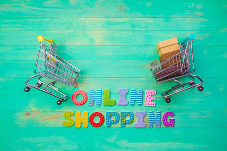 Empty and full shopping carts and inscription ONLINE SHOPPING on green wooden background. Words...