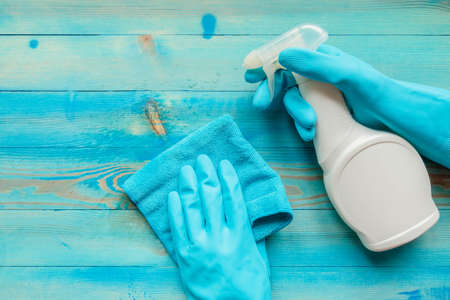 Hands in rubber gloves holding blue microfiber cleaning cloth and cleaning bottle with spraying...