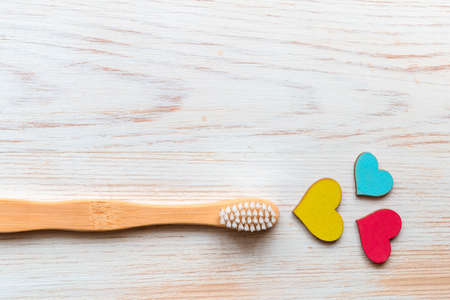 One wooden bamboo toothbrush with wooden hearts on wood background and copy space