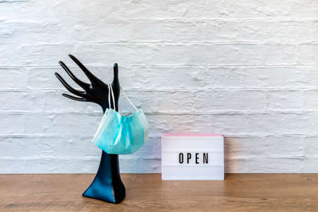 Protective facemask hanging on plastic hand and signboard OPEN. Black plastic hand holding medical...
