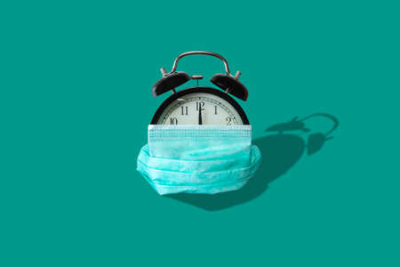 Alarm clock covered protective mask on green background