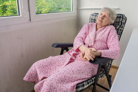 Old woman sitting on chair in terrace and looking outsideの写真素材