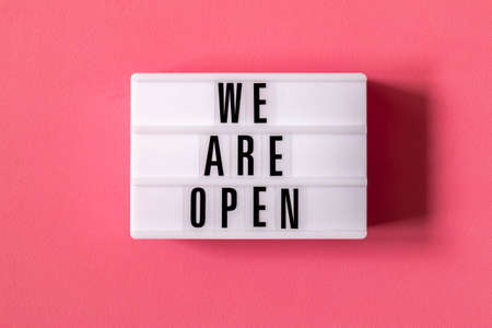 Signboard WE ARE OPEN of lightbox on red background. Open sign hanging on blue wall. Business open...
