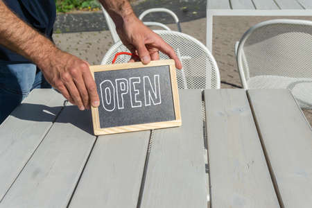 Handwritten Open sign in hands of waiter on cafe table outside. Hands holding signboard Open in open-air snack bar. Blackboard with inscription as symbol of reopened small businessの写真素材