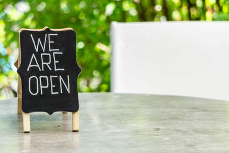 Handwritten word Open on blackboard closeup on cafe table outdoors. Open sign as symbol of reopened small business. Open sign in cafe outside inviting customersの写真素材