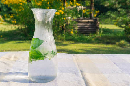 Chilled water with fresh mint in glass jug on table in countryside. Drinking water with mint leaves...