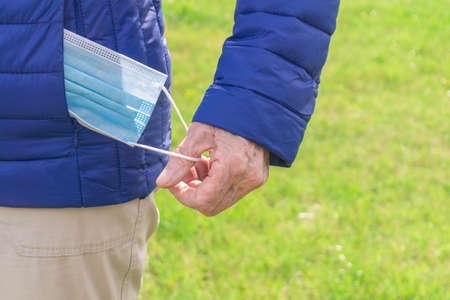 Old human hand taking out protective face mask from blue jacket pocket. Senior hand takes out of...