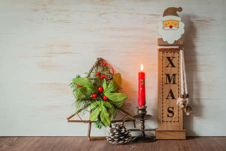 Christmas decoration of burning red candle, wooden Santa Claus, Christmas tree, baubles on table, wooden background for copy spaceの写真素材