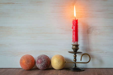 Christmas decoration. Burning red candle on candlestick and baubles on white wooden background with...