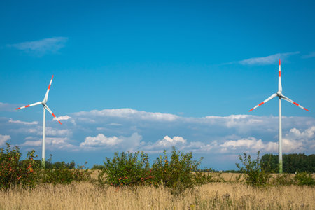 Wind turbines in meadow with apple trees on blue and cloudy sky background. Wind turbines eco farm....