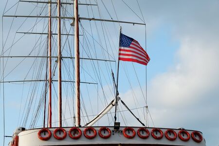 American flag waving in the strong wind off the back of a ferry boat with a blue sky with clouds background.の写真素材