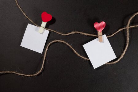 Two paper stickers attached with clothespins on a rope and hand made heart makes. valentines day black background.の写真素材