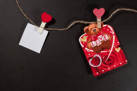 Two paper stickers attached with clothespins on a rope and hand made heart makes. valentines day black background.の写真素材